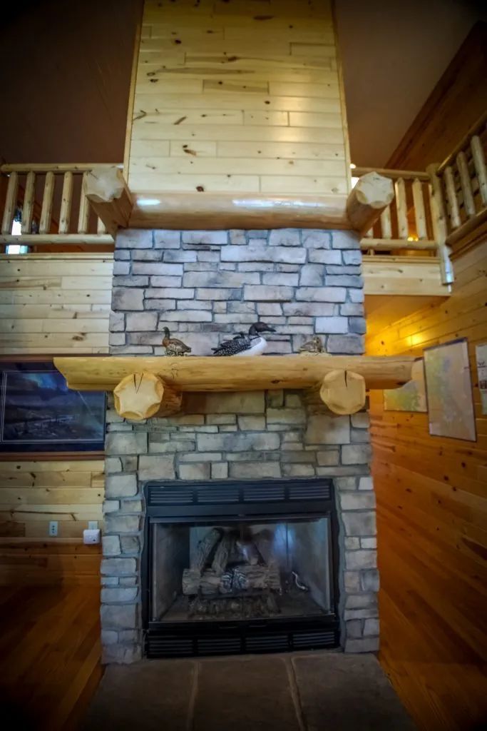 A large stone fireplace with a wooden mantle in a log cabin.