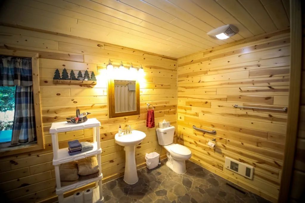 A bathroom in a log cabin with a sink , toilet and mirror.