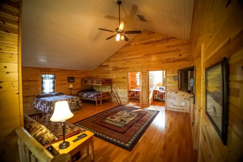 A large room in a log cabin with bunk beds and a ceiling fan.
