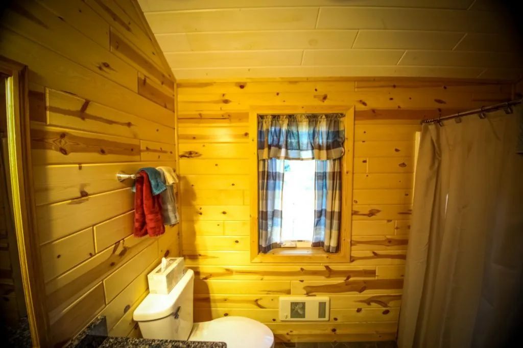 A bathroom in a log cabin with a toilet , shower and window.