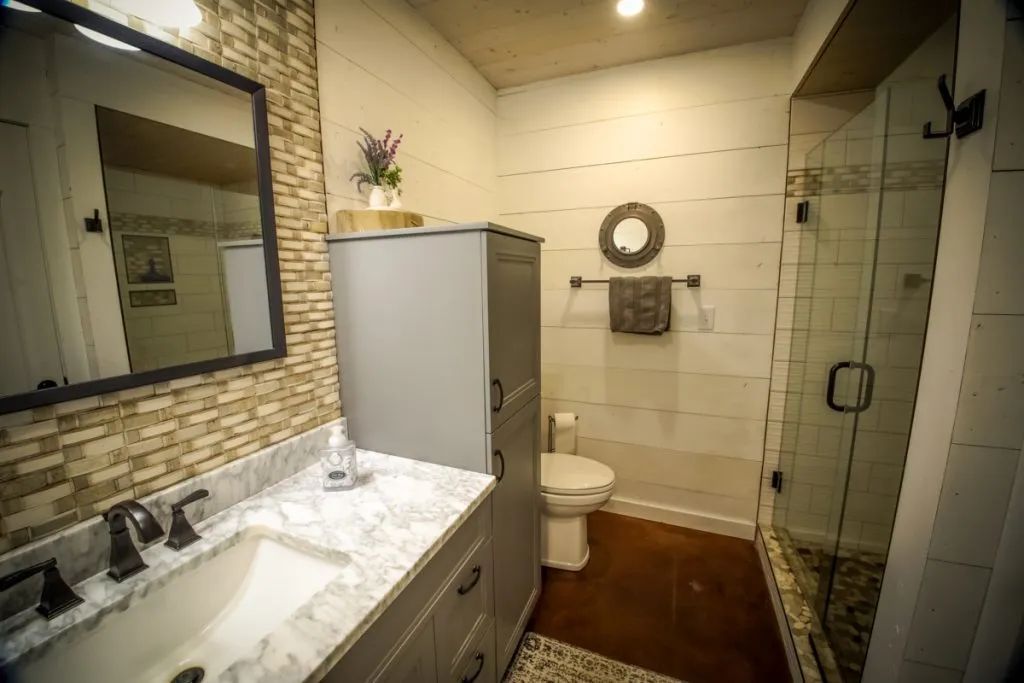 A bathroom with a sink , toilet , mirror and walk in shower.