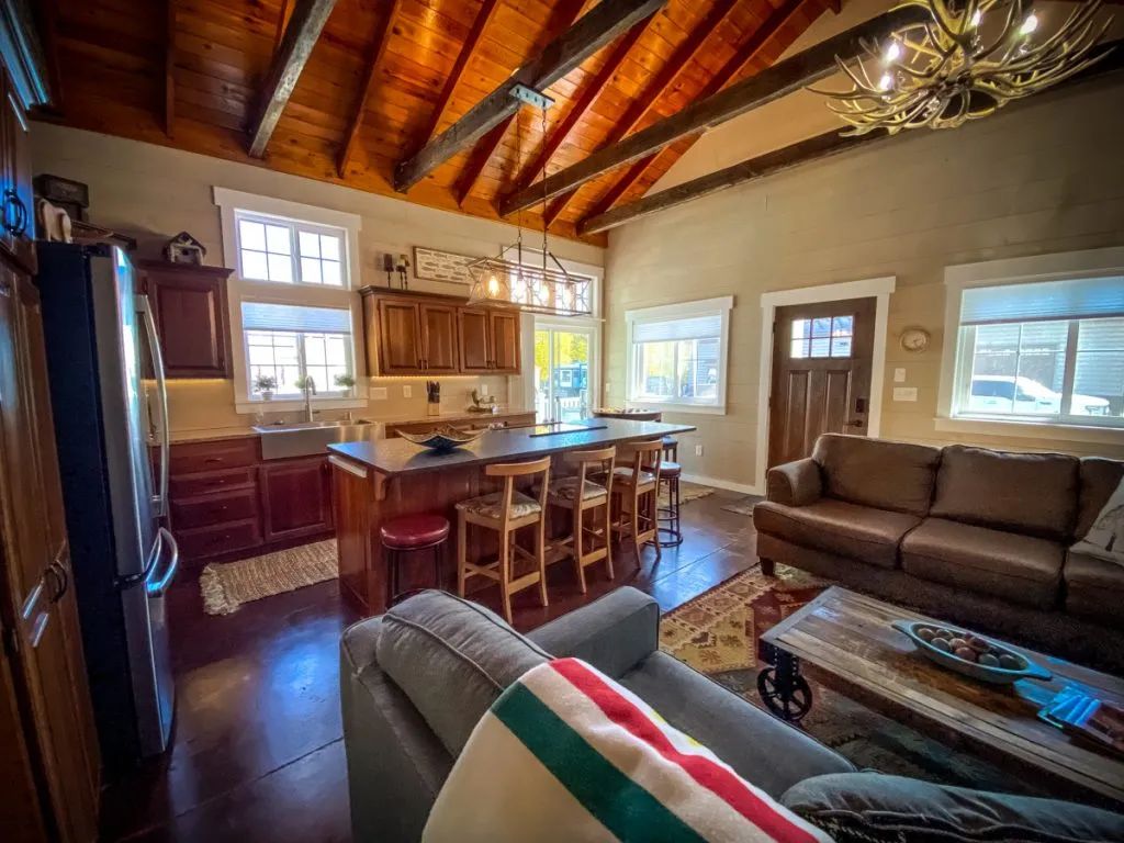 A living room filled with furniture and a kitchen with a wooden ceiling.