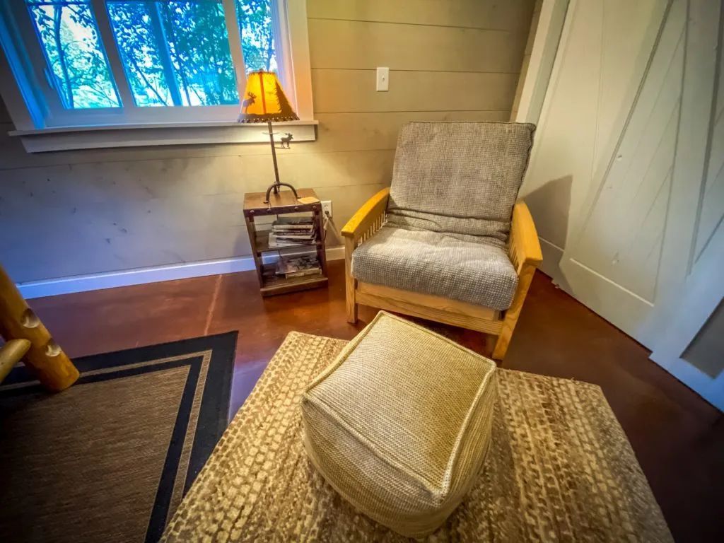 A living room with a chair , ottoman , lamp and rug.