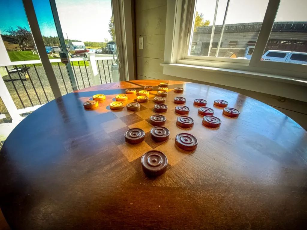 A game of checkers is being played on a wooden table in front of a window.