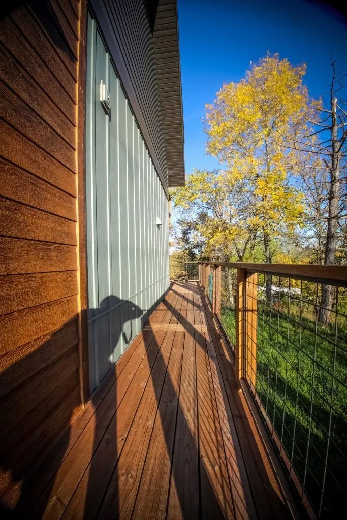 A wooden deck leading to a house with trees in the background.