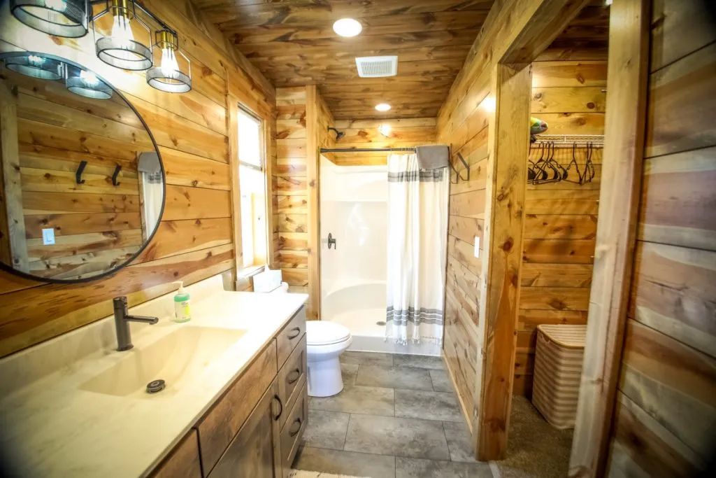A bathroom in a log cabin with a sink , toilet , shower and mirror.