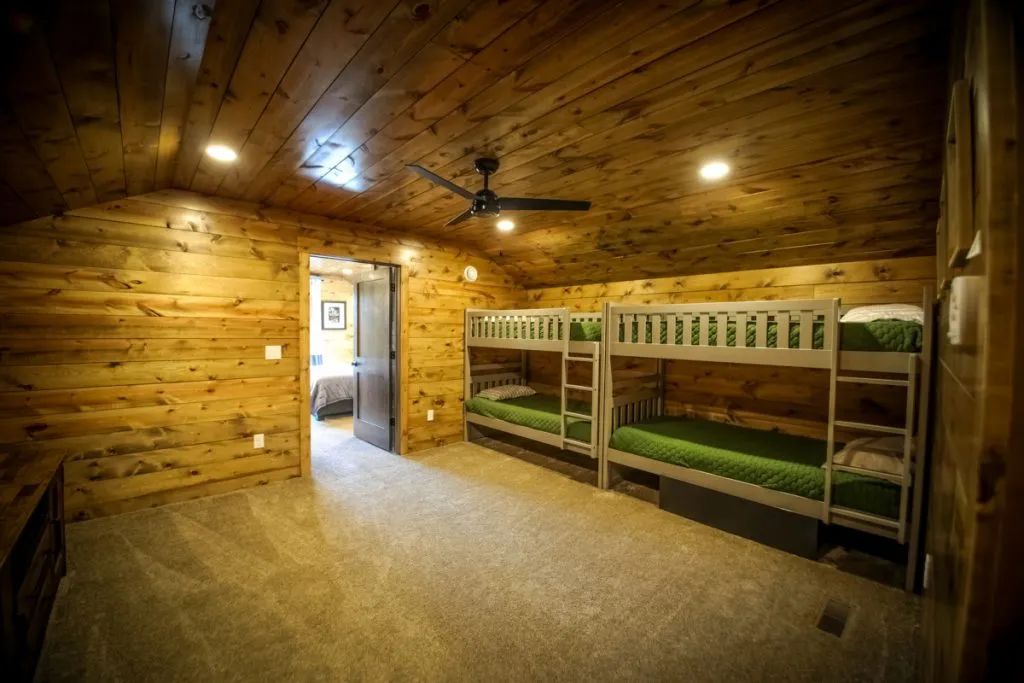 A room with bunk beds and a ceiling fan in a log cabin.