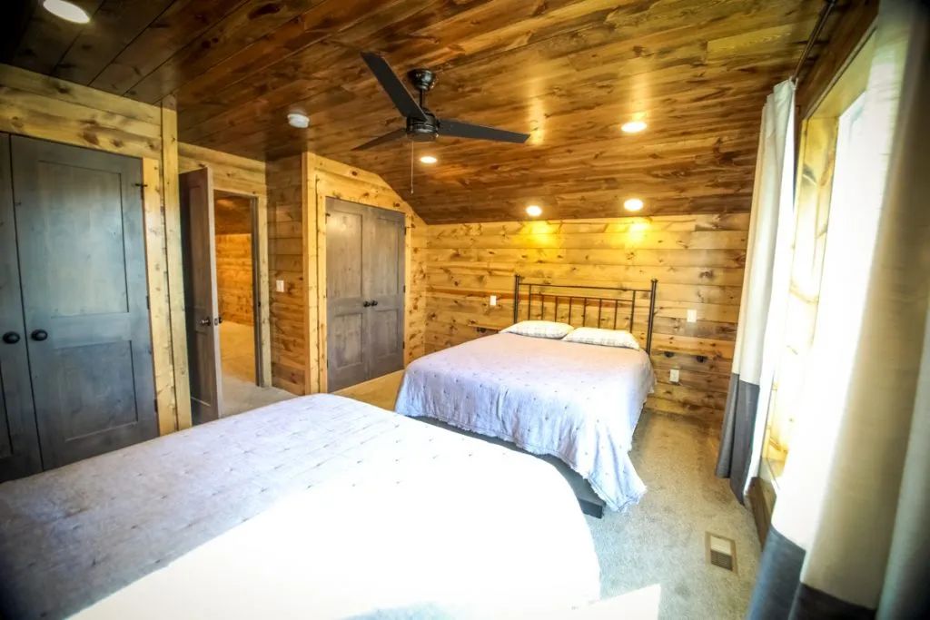 A bedroom in a log cabin with two beds and a ceiling fan.