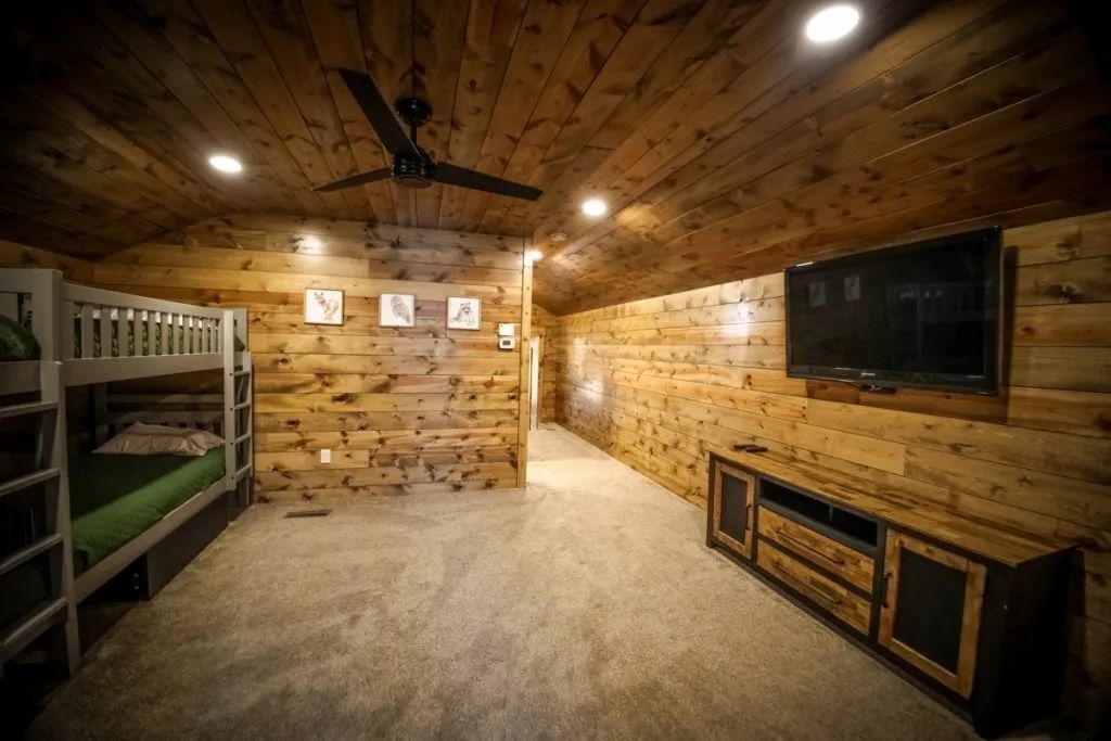 A room with bunk beds , a flat screen tv and a ceiling fan.