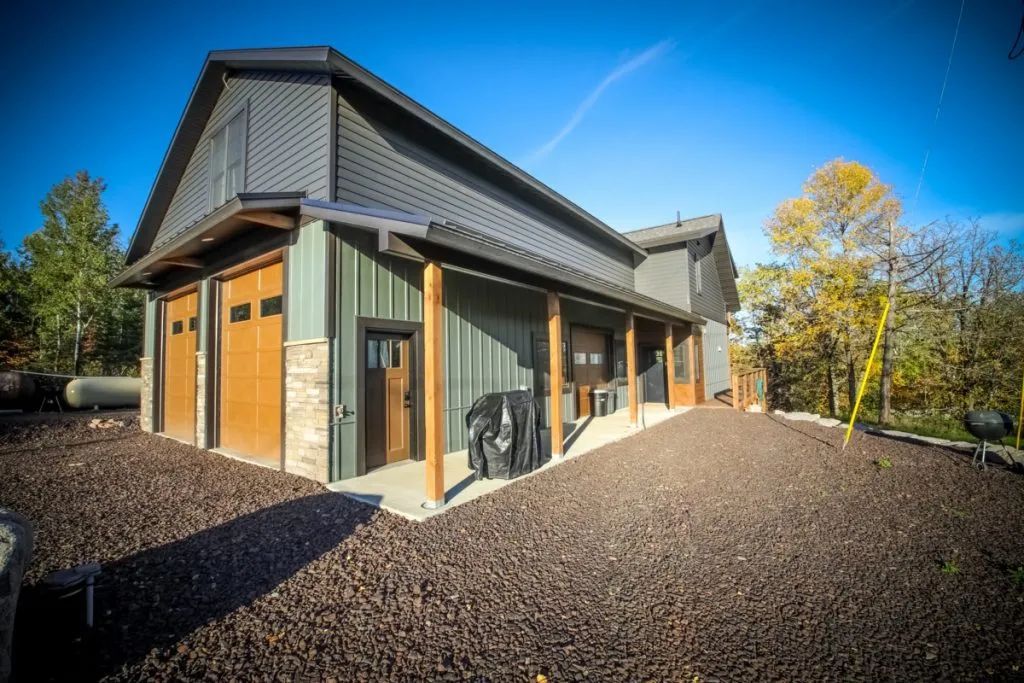 A large house with a garage and a porch is sitting on top of a dirt hill.