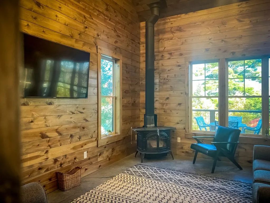 A living room in a log cabin with a wood stove and a flat screen tv.