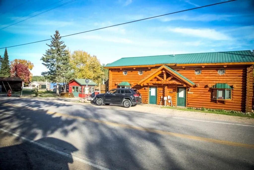 A car is parked in front of a log cabin.