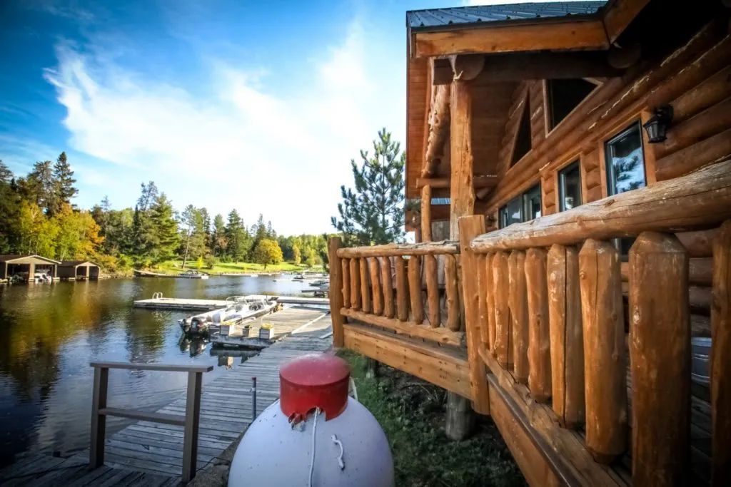 A log cabin with a propane tank in front of it and a lake in the background.