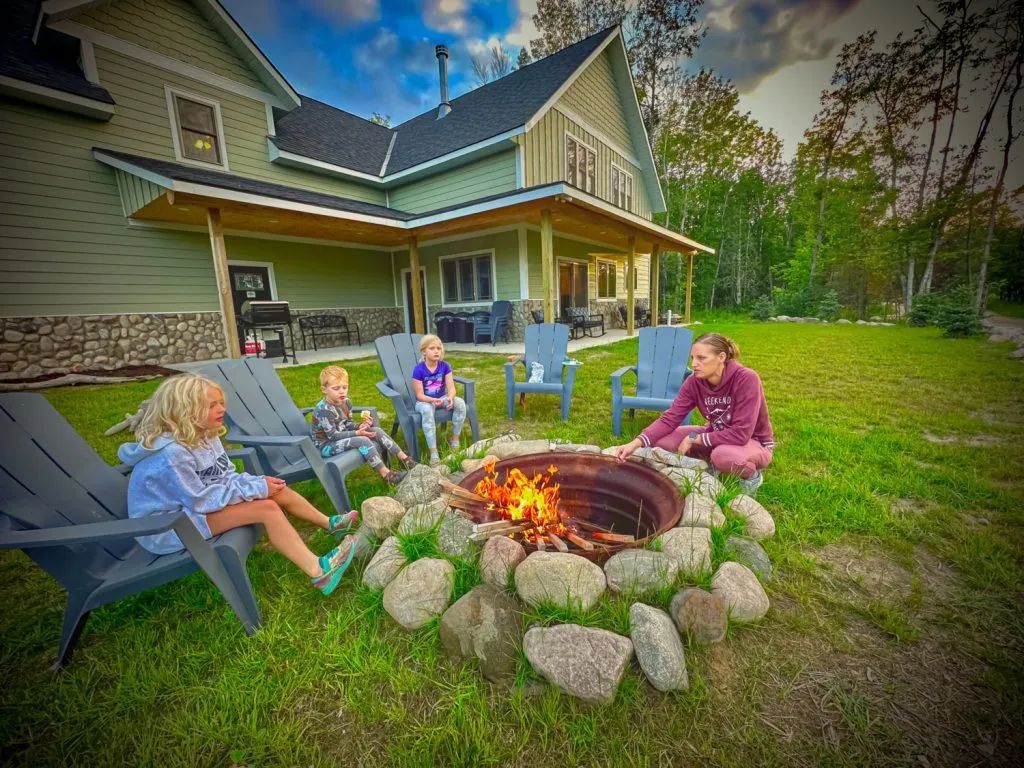 A group of children are sitting around a fire pit in front of a house.