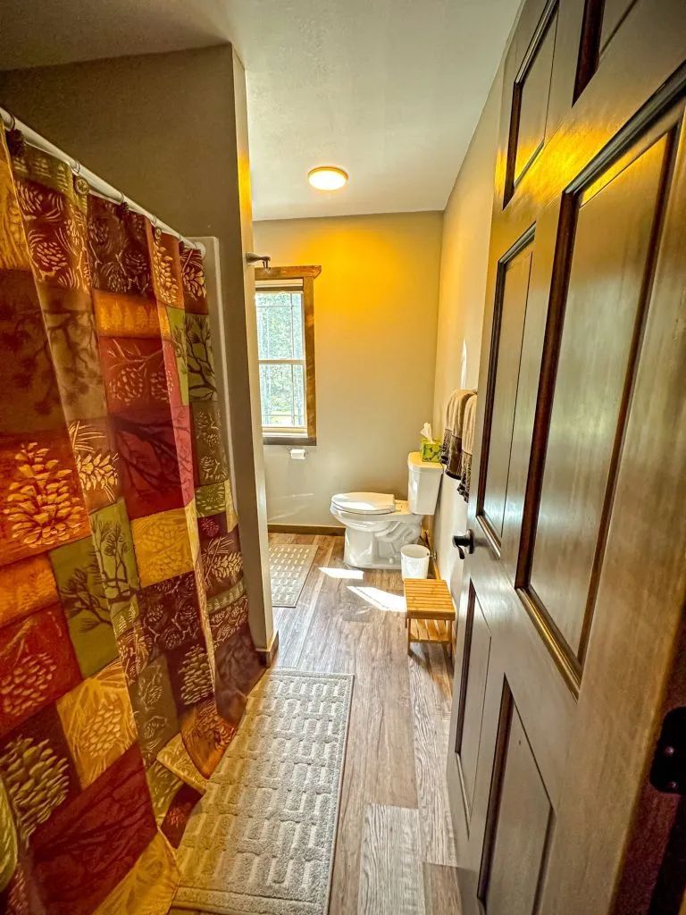 A bathroom with a toilet , shower curtain , and window.