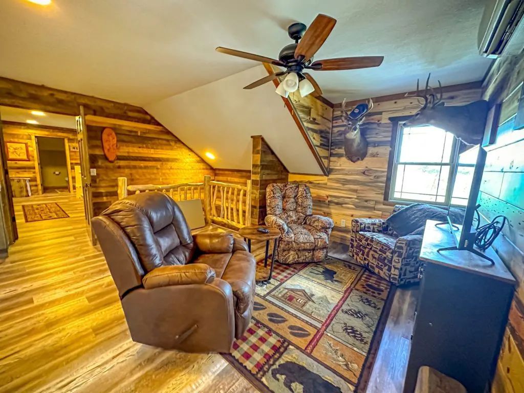 A living room in a log cabin with a ceiling fan and chairs.