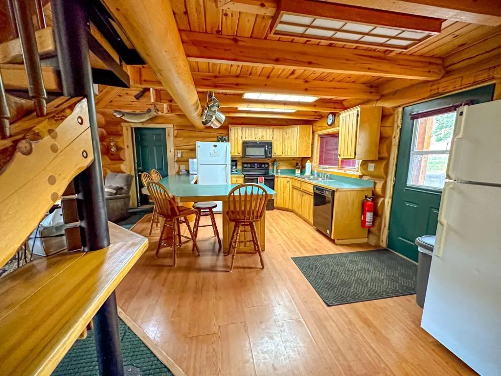A kitchen in a log cabin with a table and chairs and a refrigerator.
