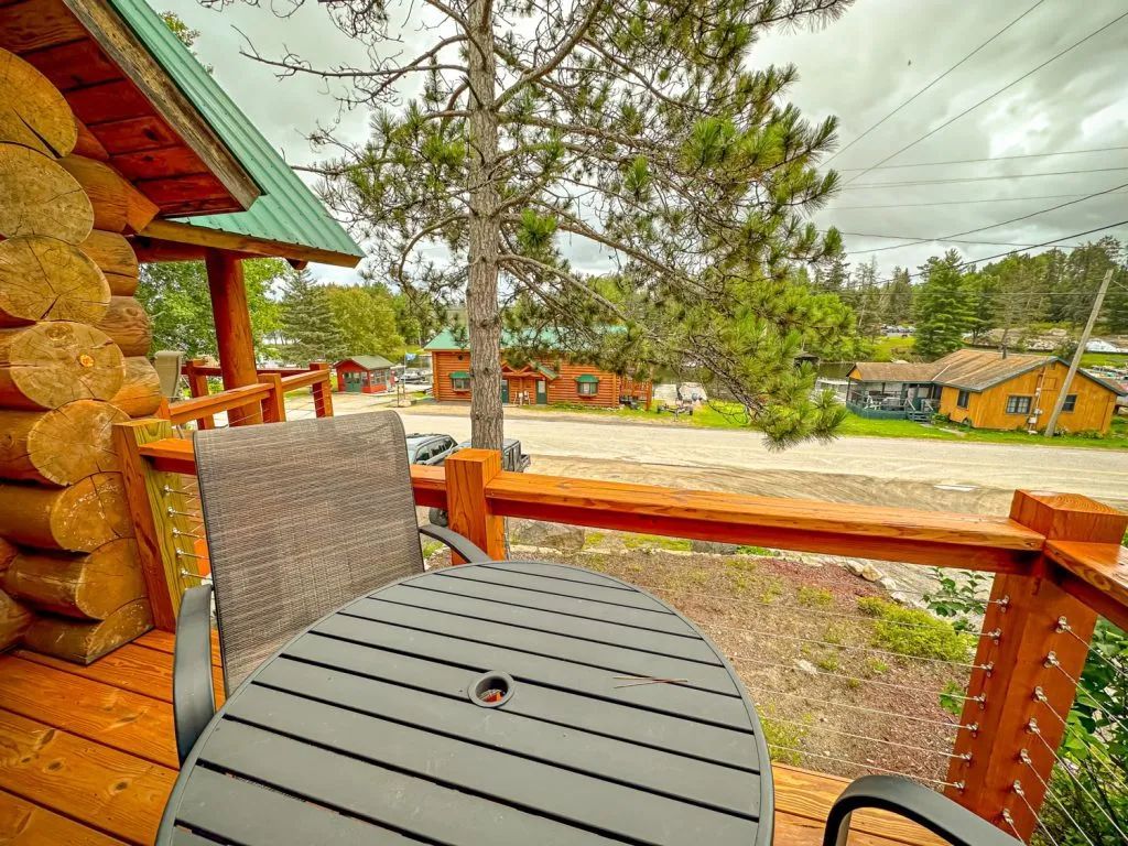 There is a table and chairs on the deck of a log cabin.