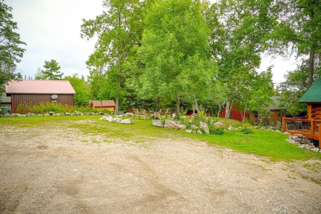 A dirt road leading to a log cabin in the middle of a lush green field.