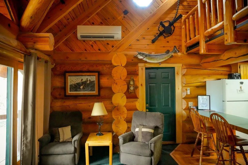 A living room in a log cabin with two chairs and a table.