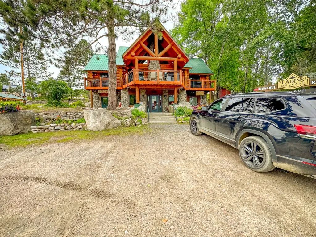A car is parked in front of a large log cabin.