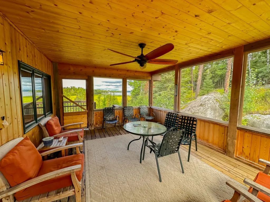 A screened in porch with a table and chairs and a ceiling fan.
