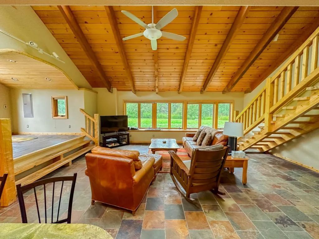 A living room with a couch , chairs , stairs and a ceiling fan.