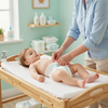 A person changes a baby's diaper on a wooden changing table in a nursery.