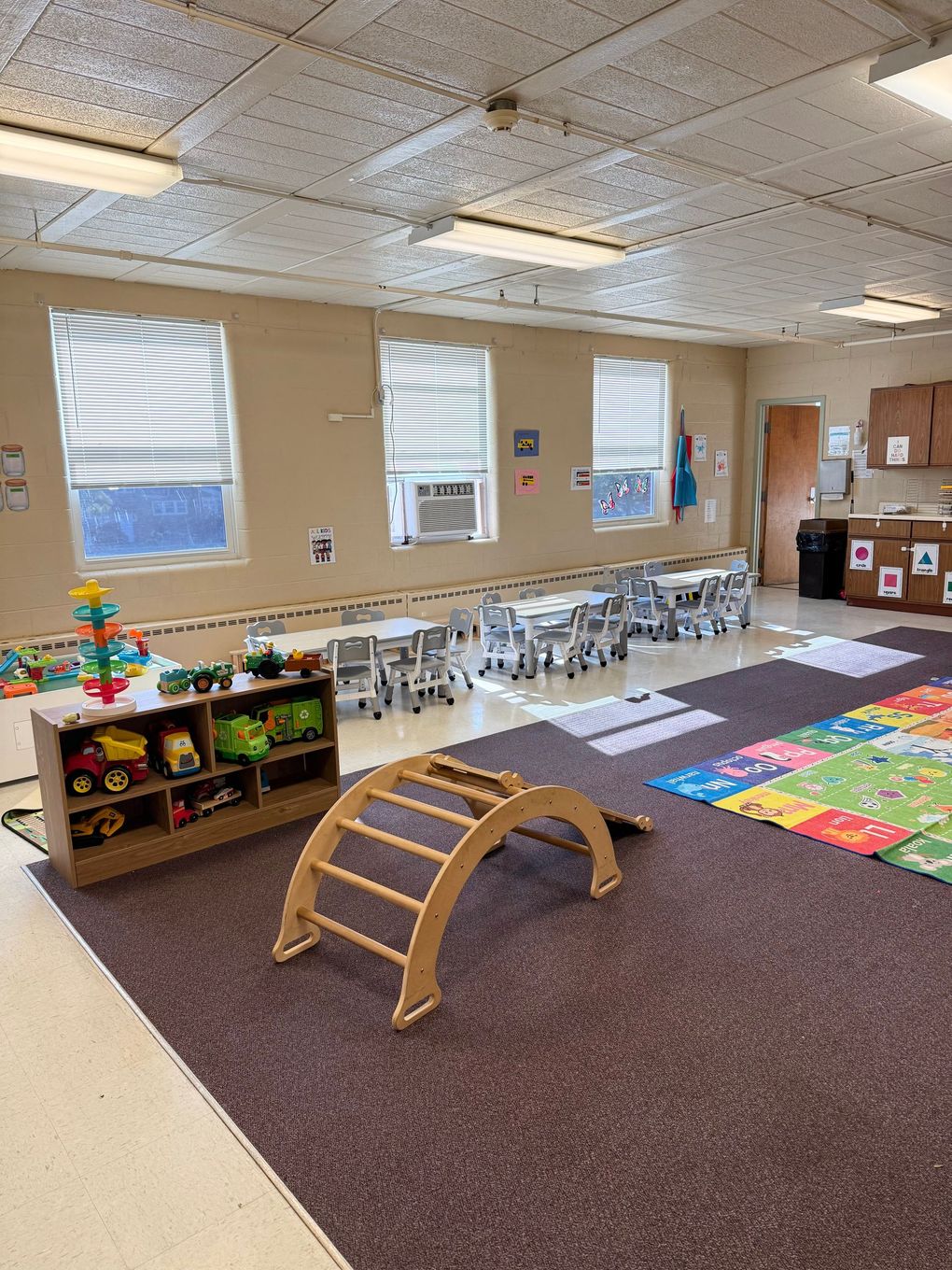 Four children sit at a table in a classroom, focused on cutting and folding colorful construction paper for a craft project.