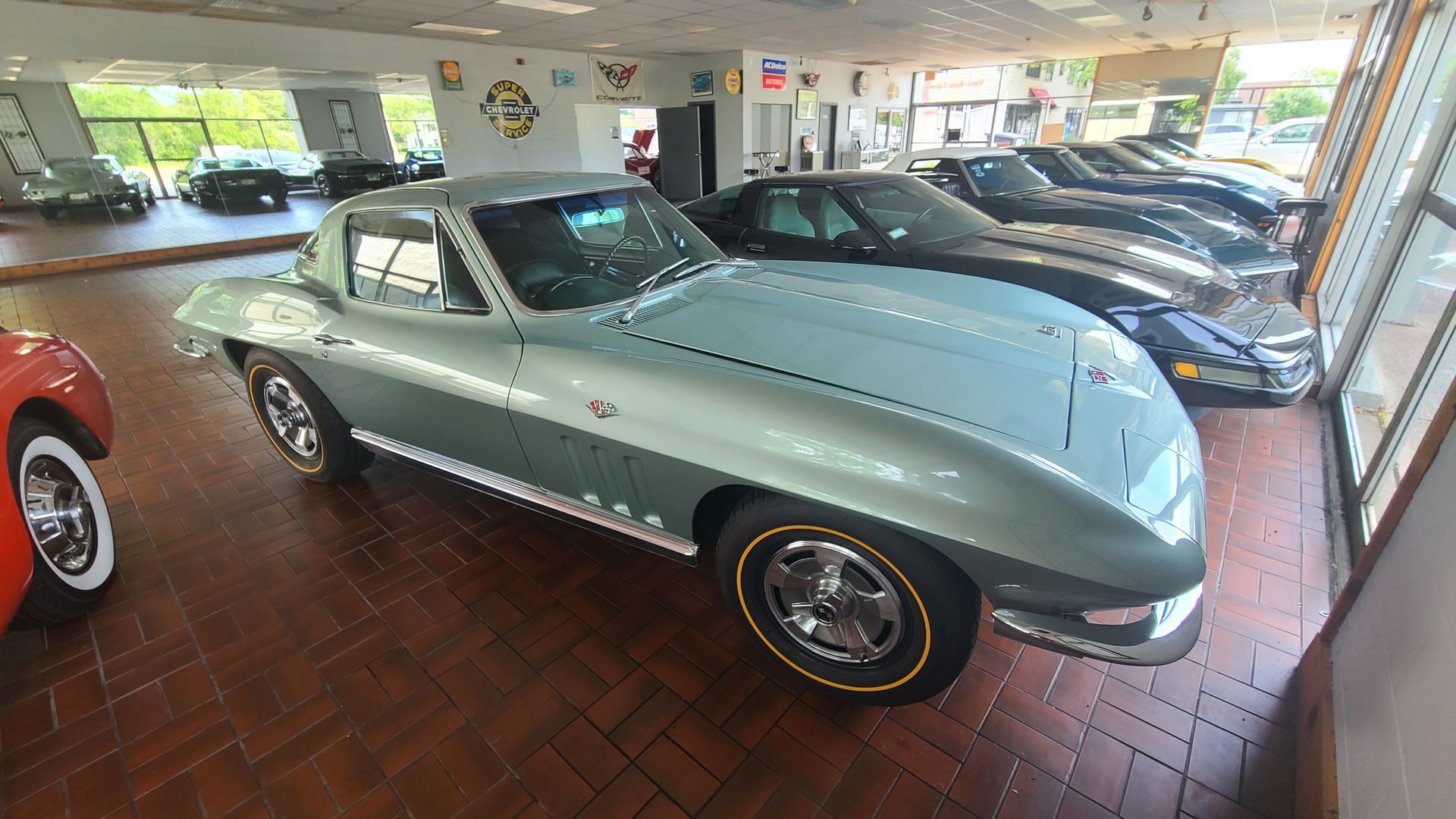 A corvette is parked in a showroom next to other cars.
