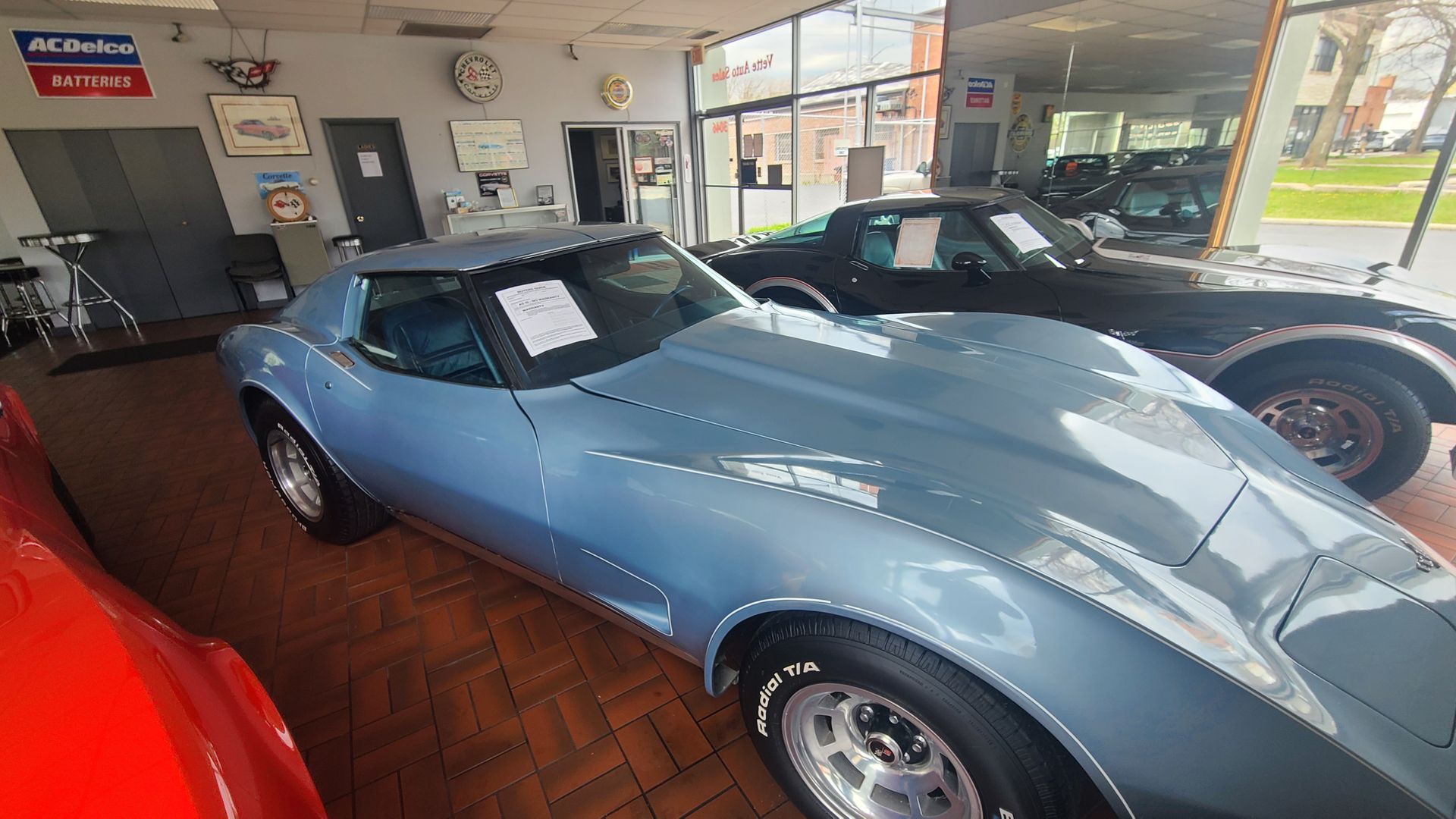 A blue corvette is parked in a showroom next to a black corvette.
