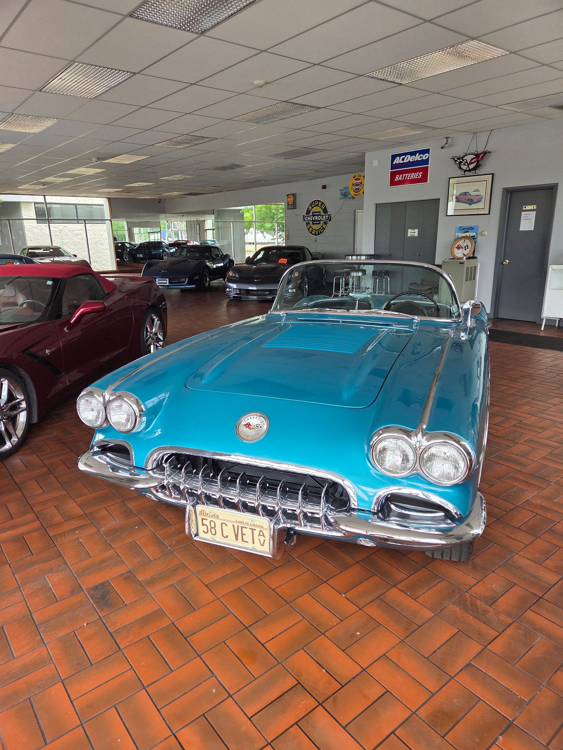 Turquoise classic convertible car displayed indoors on a tiled showroom floor.