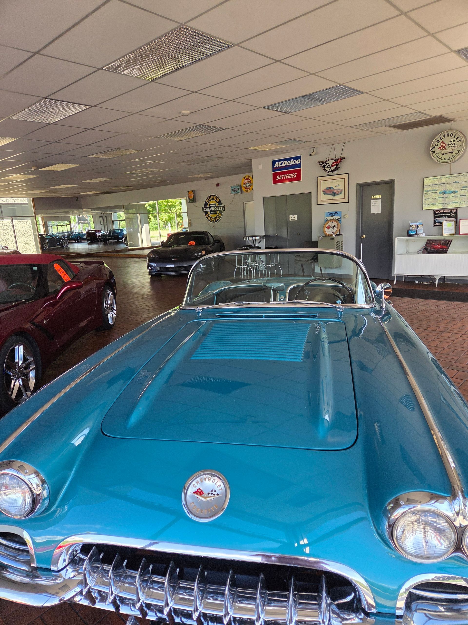 Classic turquoise convertible parked inside a showroom with other cars in the background