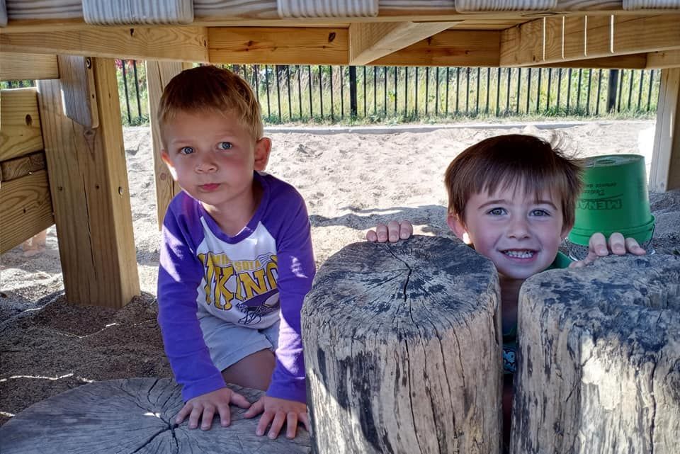 Two young boys are playing under a wooden structure