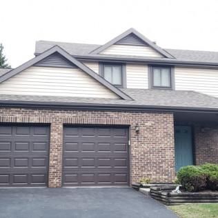 Suburban brick house with two garage doors, gray siding, and a small front lawn