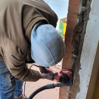 Worker using a red power tool to cut into a brick wall at a construction site