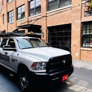 White utility pickup truck parked beside a brick building in an alleyway