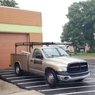 Silver utility pickup truck with roof rack parked in front of a tan building
