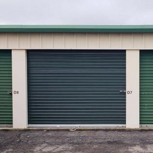 Row of storage unit doors, with green and blue metal roll-up doors on a concrete lot