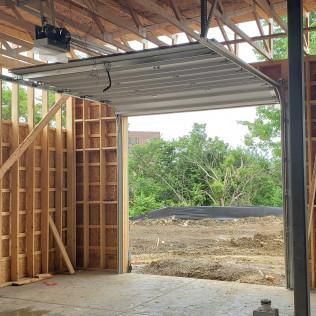 Partially open garage under construction with raised door, wooden framing, and view of trees outside