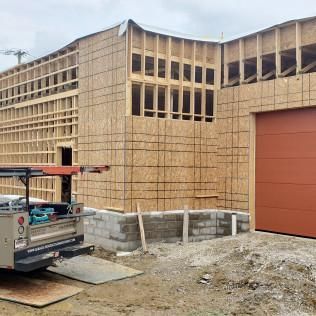 Construction site with partially built wood-framed building, truck, and red garage door