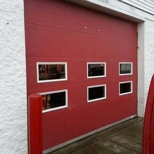Red garage door with five small windows set in a white wall.