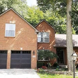 Brick suburban house with black garage door, front porch, and large tree in the yard