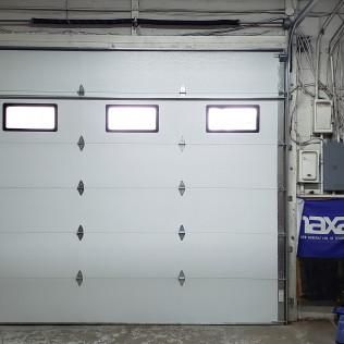 Closed white garage door with three small windows in an industrial interior