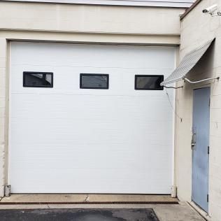White garage door with three small windows beside a blue door and awning.