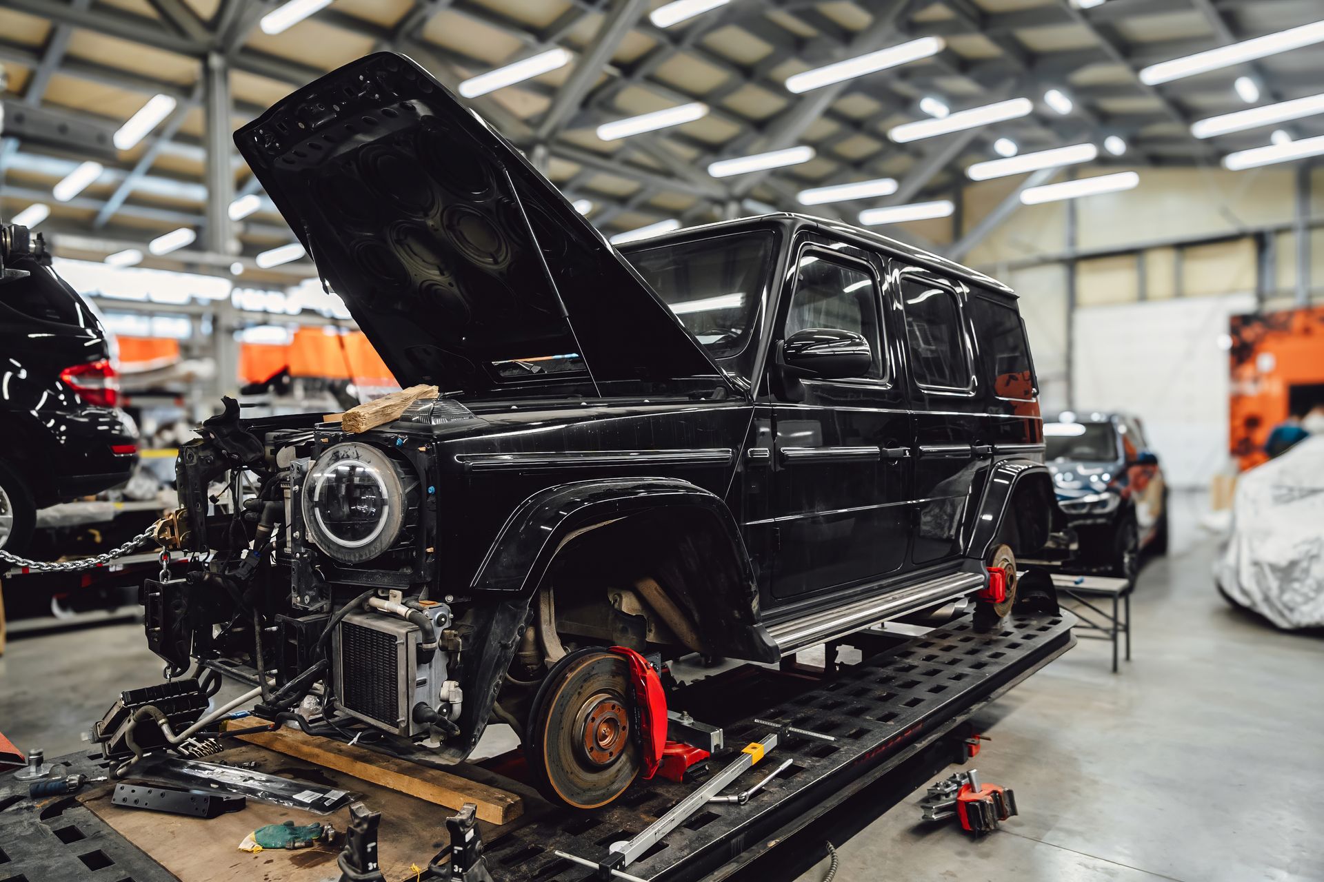 Black car under repair in an auto shop, hood open and parts removed on a lift