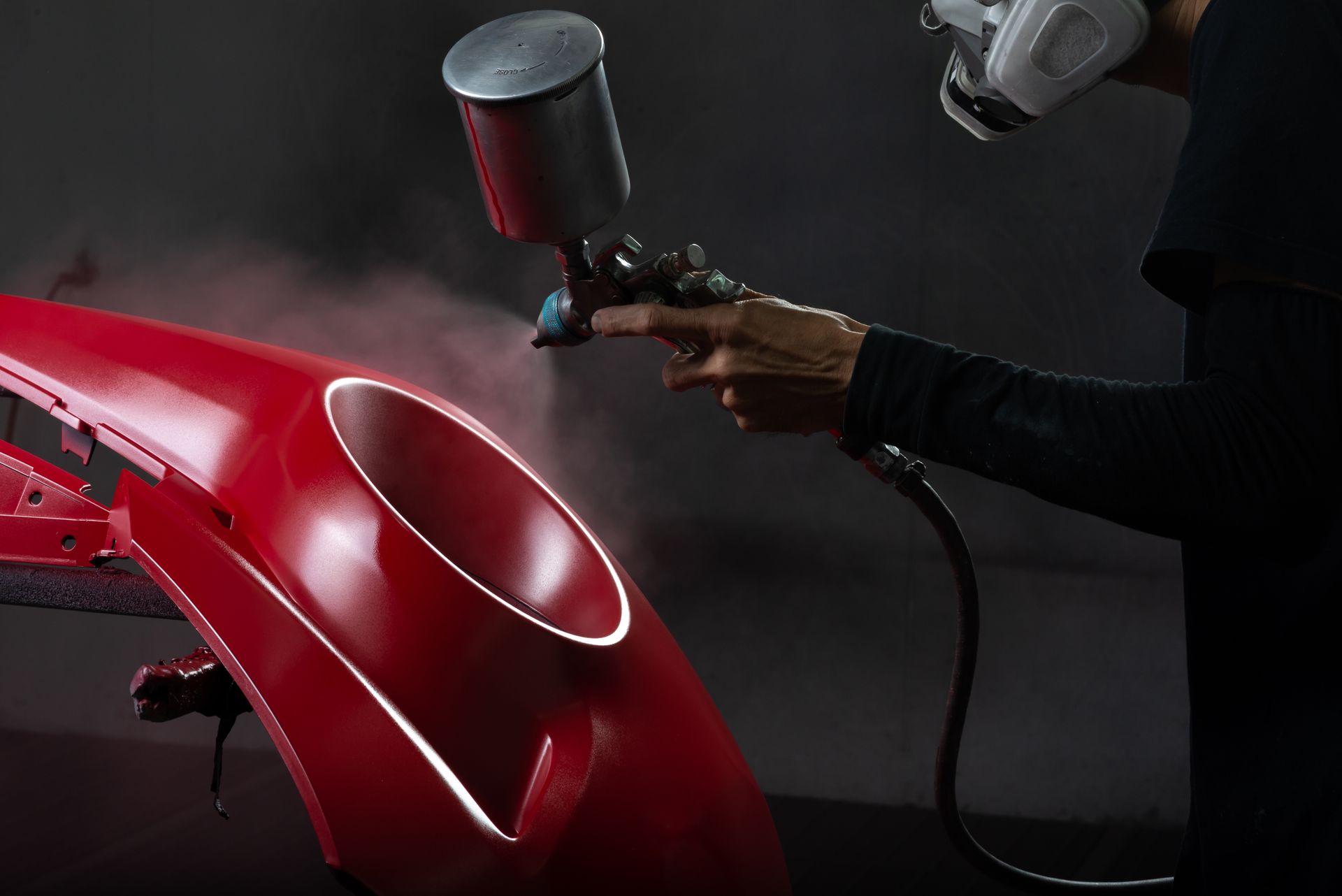 Person spray-painting a red car body with a paint gun in a workshop