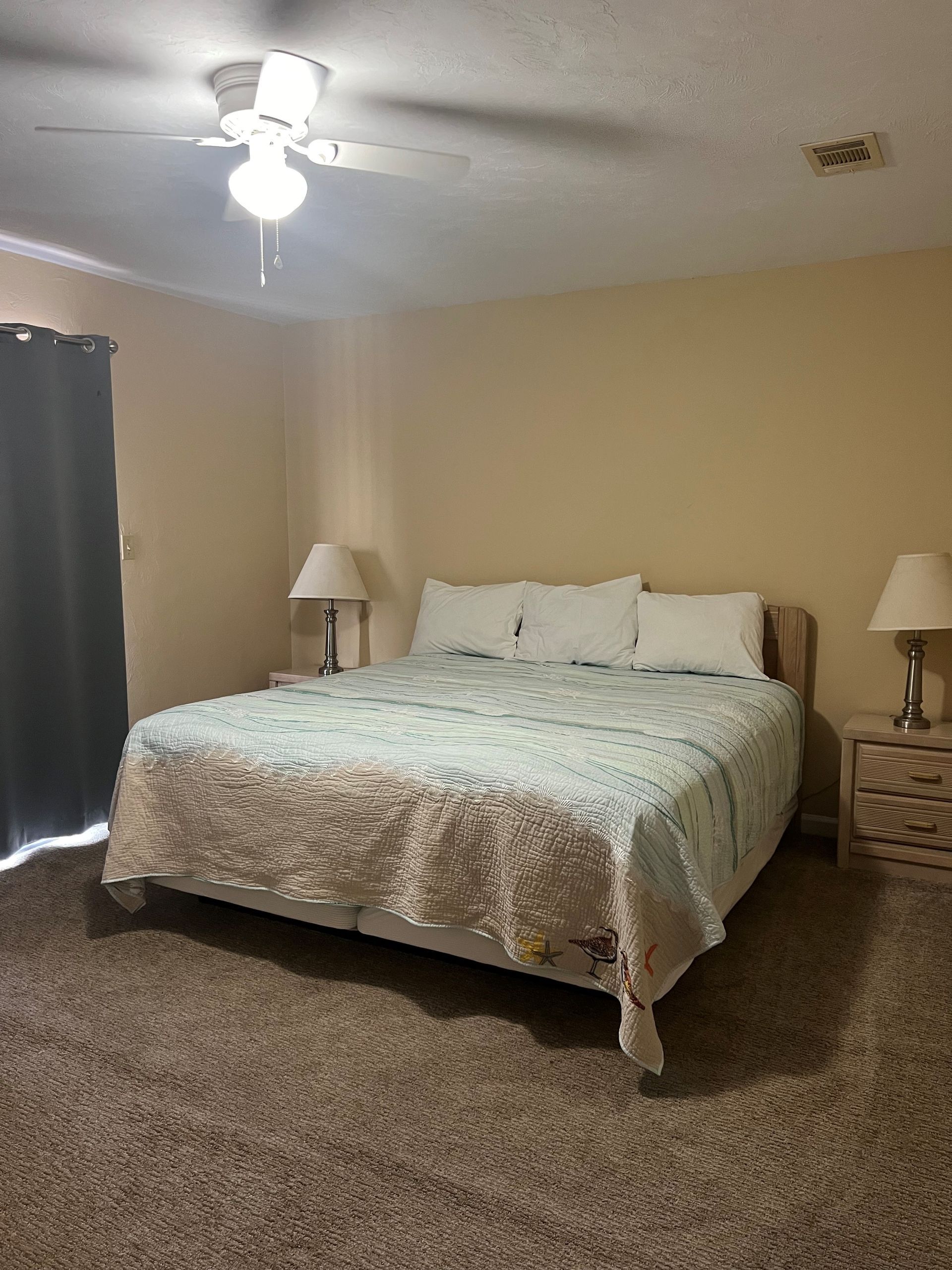 A bedroom with a king size bed , two lamps , and a ceiling fan.