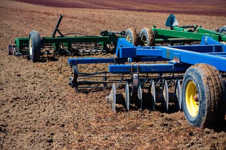Blue and green farm tillage implements parked in a dry field Blue and green farm tillage implements parked in a dry field