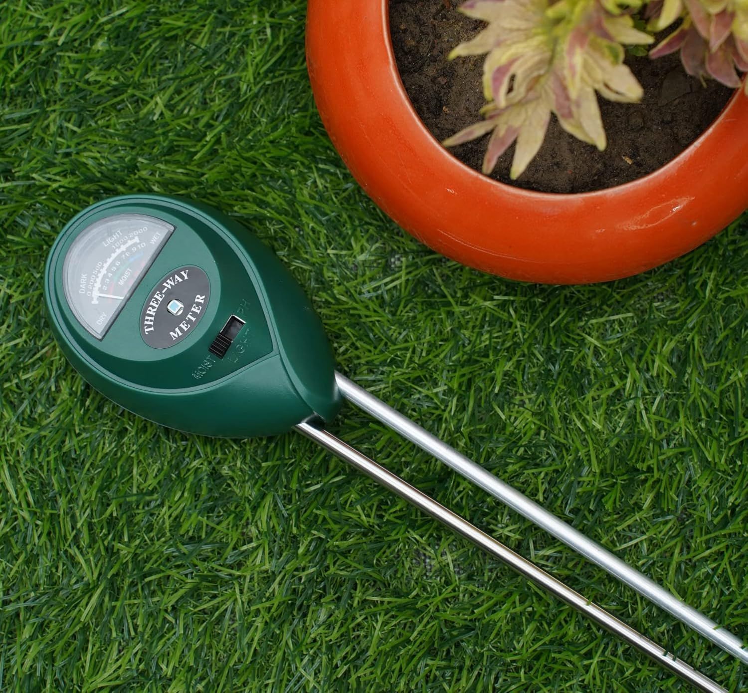 A soil moisture meter is sitting on top of a lush green lawn next to a potted plant.